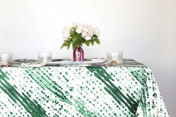 Glissando shibori 100% cotton tablecloth in verdant emerald green on table with full place settings, mosaic garden dinner plates, hand-painted confetti glasses, and a hand-painted vase with roses against a white background 