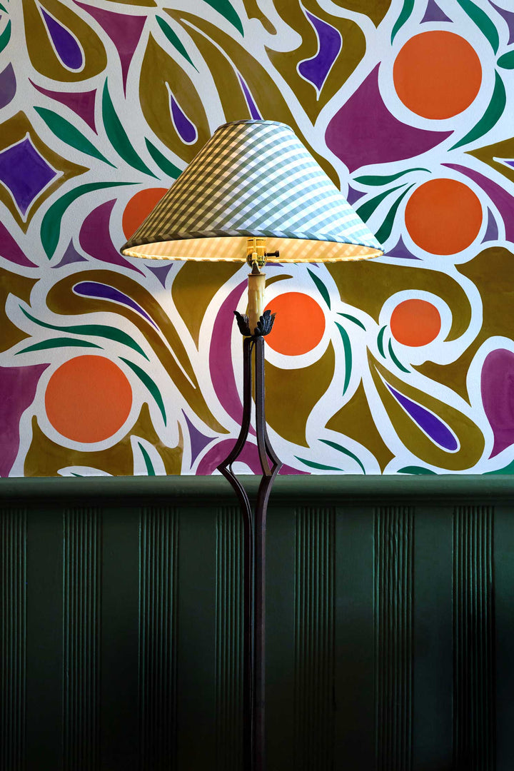 Venable Moore made to order Capri abstract floral wallpaper in orange, purple, and brown on wall with green wainscotting and lamp with checkered shade