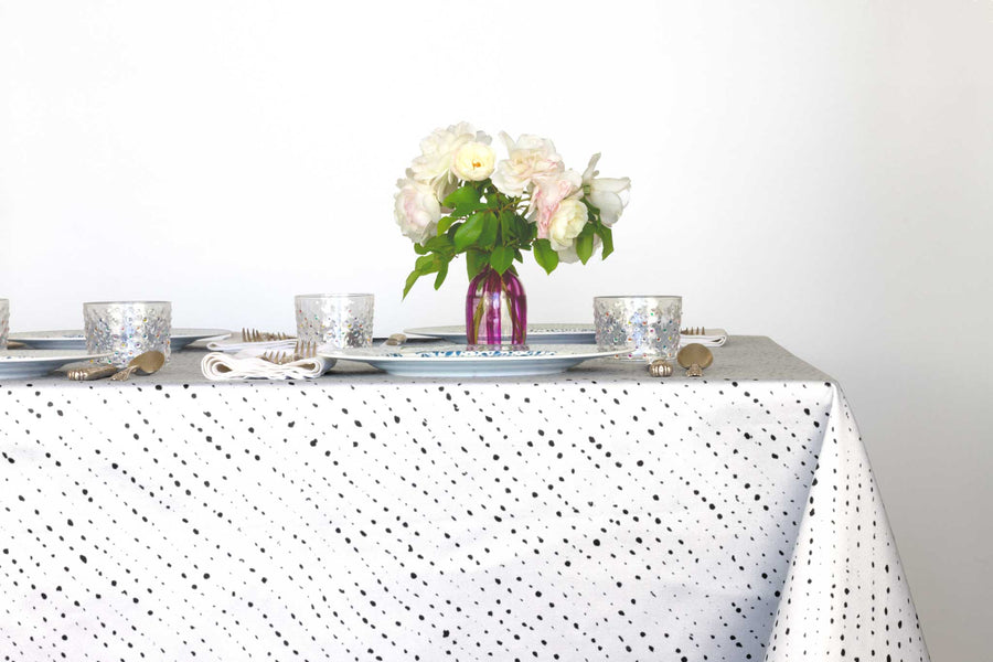 Staccato Nero shibori 100% cotton tablecloth in creamy alabaster white on table with full place settings, mosaic garden dinner plates, hand-painted confetti glasses, and a hand-painted vase with roses against a white background 