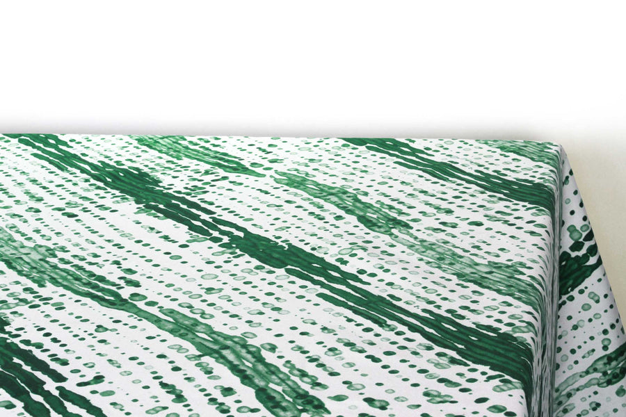 Glissando  shibori 100% cotton tablecloth in verdant emerald green on table corner view against a white background