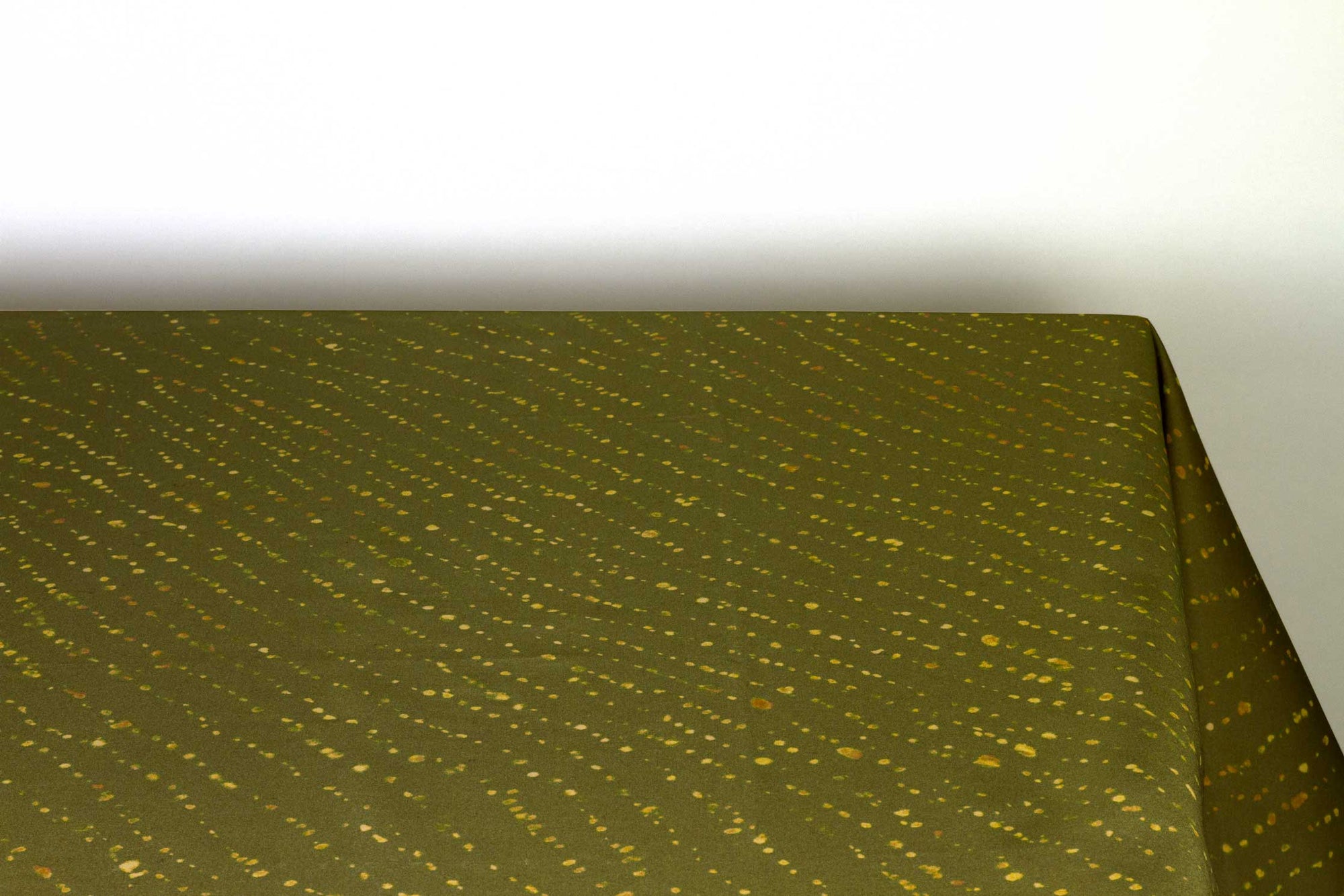 Staccato decolorato shibori 100% cotton tablecloth in earthy fern green on table against a white background