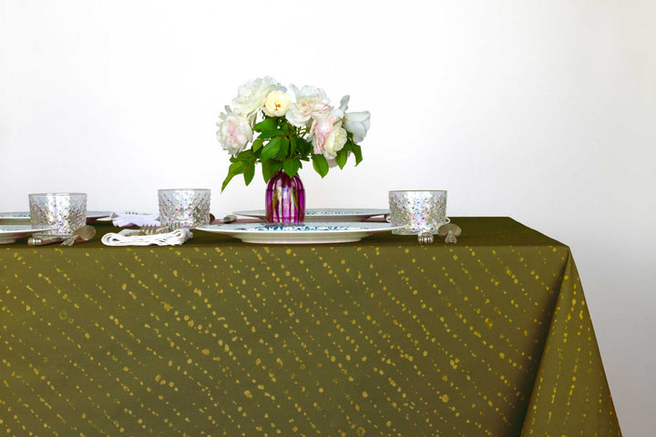 Staccato decolorato shibori 100% cotton tablecloth in earthy fern green on table with full place settings, mosaic garden dinner plates, hand-painted confetti glasses, and a hand-painted vase with roses against a white background 