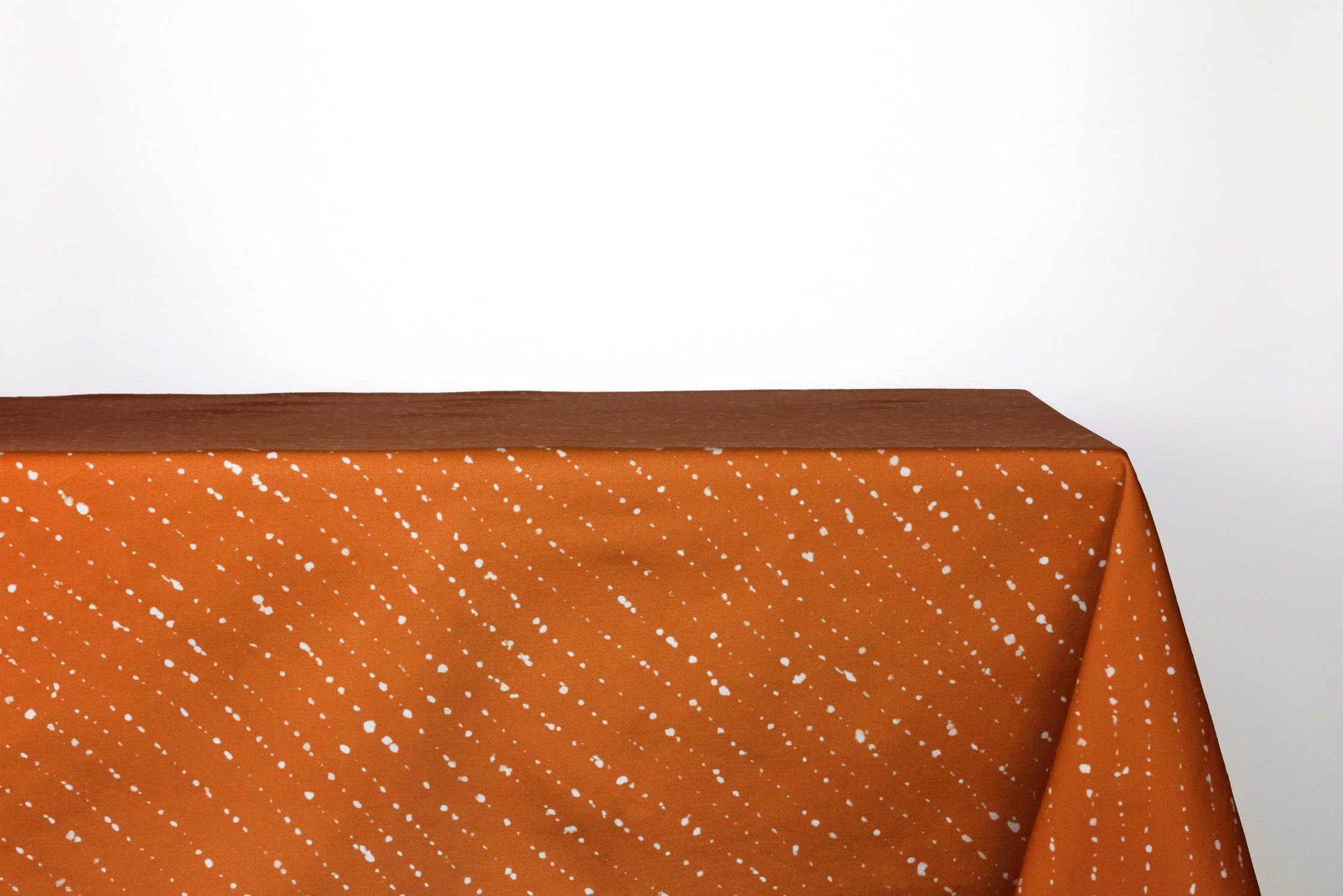 Staccato sbiancato shibori 100% cotton tablecloth in earthy ginger orange on table against a white background 