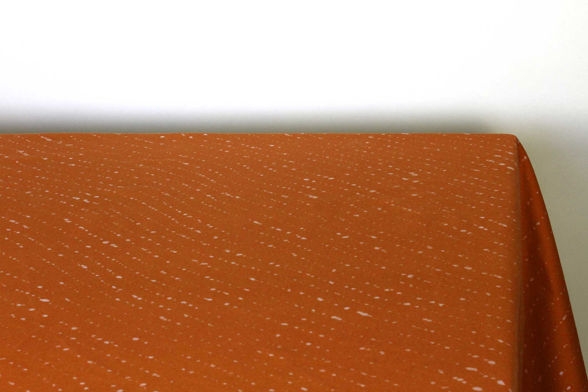 Staccato sbiancato shibori 100% cotton tablecloth in earthy ginger orange on table corner view against a white background 