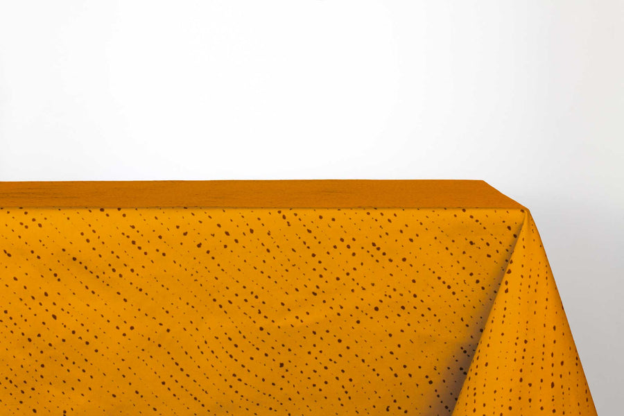 Staccato Nero shibori 100% cotton tablecloth in bold marigold yellow on table against a white background