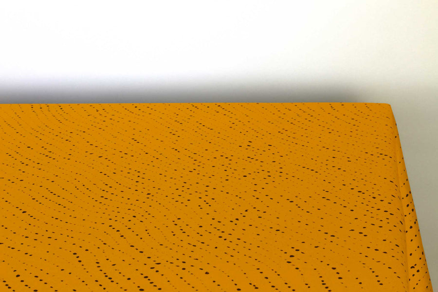 Staccato Nero shibori 100% cotton tablecloth in bold marigold yellow on table corner view against a white background