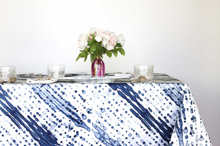 Glissando shibori 100% cotton tablecloth in navy marine blue on table with full place settings, mosaic garden dinner plates, hand-painted confetti glasses, and a hand-painted vase with roses against a white background 