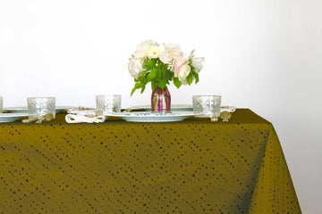 Staccato Nero shibori 100% cotton tablecloth in grounding moss green on table with full place settings, mosaic garden dinner plates, hand-painted confetti glasses, and a hand-painted vase with roses against a white background 