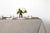  Staccato sbiancato shibori 100% cotton tablecloth in neutral flax tan on table with full place settings, mosaic garden dinner plates, hand-painted confetti glasses, and a hand-painted vase with roses against a white background