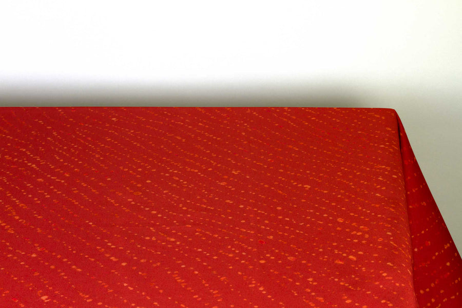 Staccato decolorato shibori 100% cotton tablecloth in vibrant paprika red on table corner view against a white background 