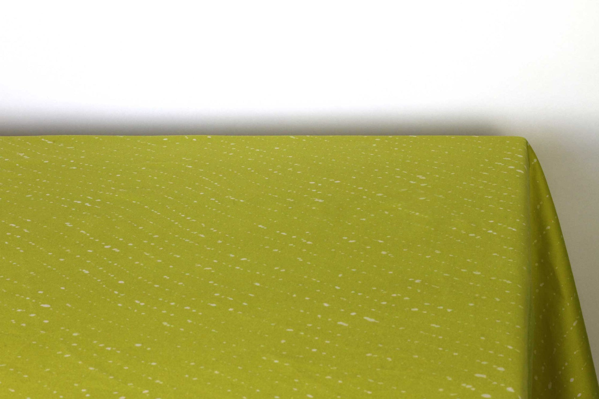 Staccato sbiancato shibori 100% cotton tablecloth in juicy pear green on table corner view against a white background 