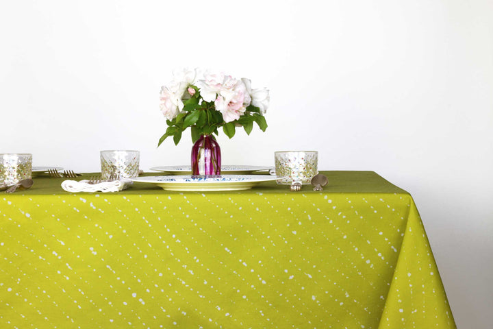 Staccato sbiancato shibori 100% cotton tablecloth in juicy pear green on table with full place settings, mosaic garden dinner plates, hand-painted confetti glasses, and a hand-painted vase with roses against a white background