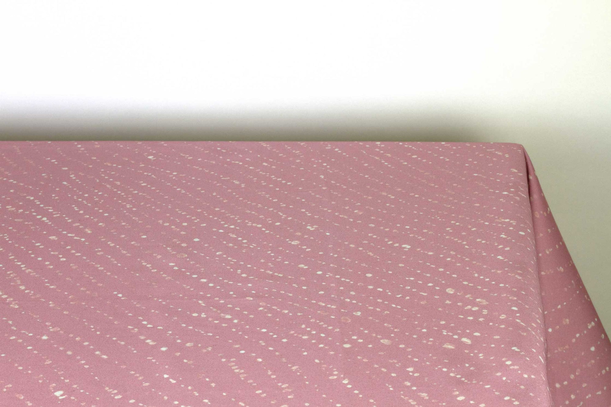 Staccato decolorato shibori 100% cotton tablecloth in dusty rose clay pink on table corner view against a white background
