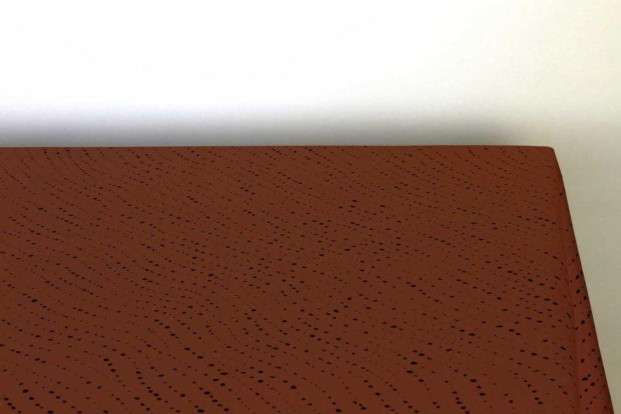 Staccato Nero shibori 100% cotton tablecloth in rich russet brown on table corner view against a white background
