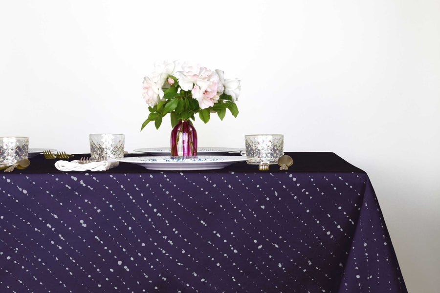 Staccato sbiancato shibori 100% cotton tablecloth in vibrant sapphire blue on table with full place settings, mosaic garden dinner plates, hand-painted confetti glasses, and a hand-painted vase with roses against a white background 