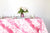 Glissando shibori 100% cotton tablecloth in juicy strawberry pink on table with full place settings, mosaic garden dinner plates, hand-painted confetti glasses, and a hand-painted vase with roses against a white background