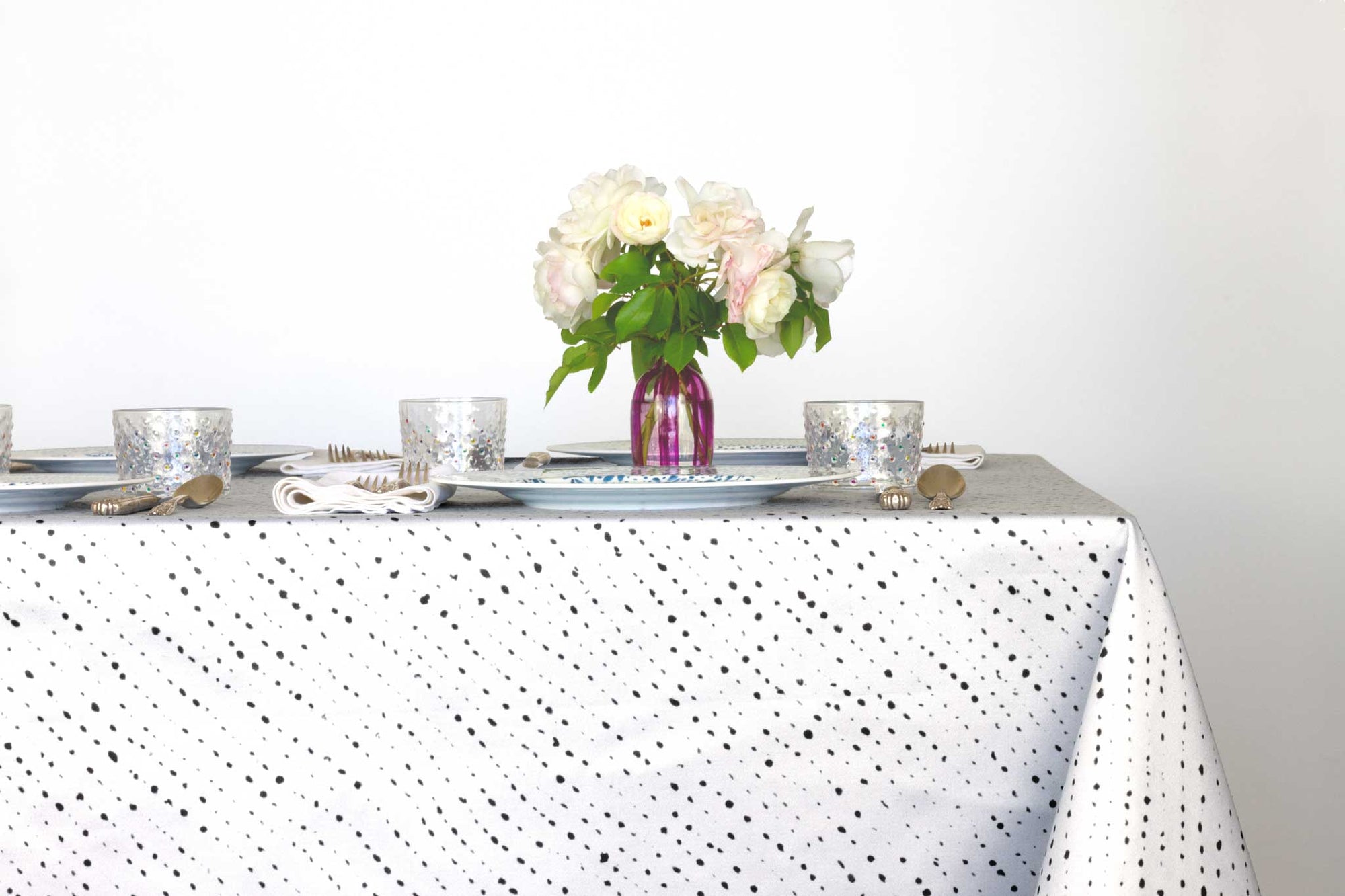 Venable Moore Staccato Nero shibori 100% cotton tablecloth in creamy alabaster white on table with full place settings, mosaic garden dinner plates, hand-painted confetti glasses, and a hand-painted vase with roses against a white background 