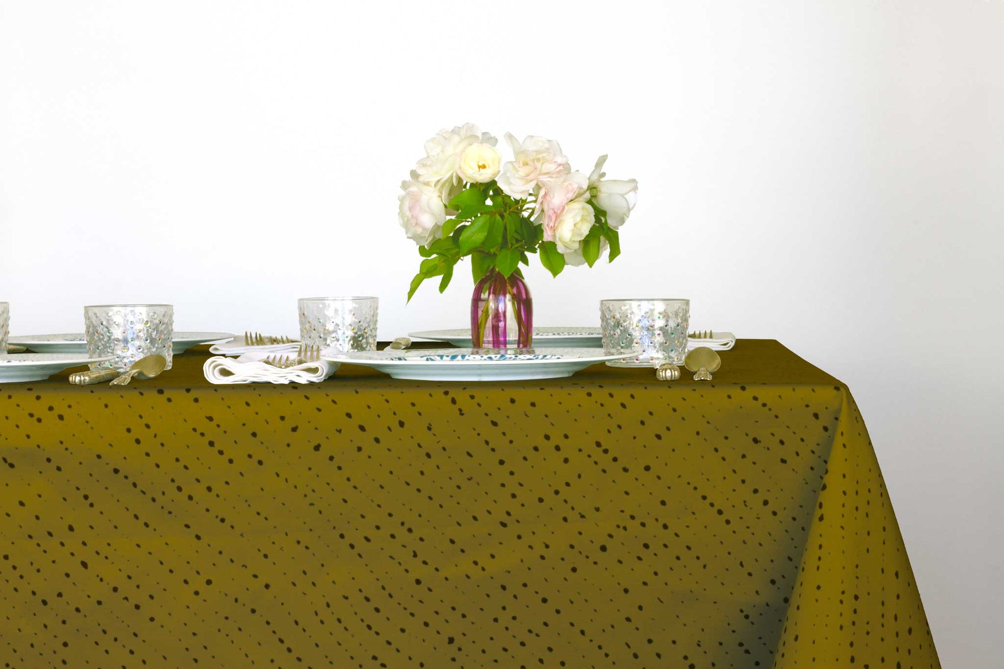 Venable Moore Staccato Nero shibori 100% cotton tablecloth in grounding moss green on table with full place settings, mosaic garden dinner plates, hand-painted confetti glasses, and a hand-painted vase with roses against a white background 