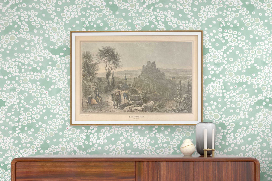 Venable Moore ‘Frizzante’ Pastel verdigris green made-to-order, printed in the U.S.A. wallpaper on a wall with wood console, vases, and framed art