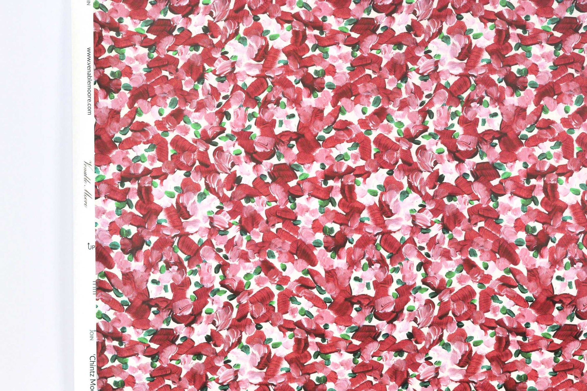 Up close view of Venable Moore Chintz Modern floral abstract in cherry pink, red, and white FSC Certified Clay Coated wallpaper roll against a white wall