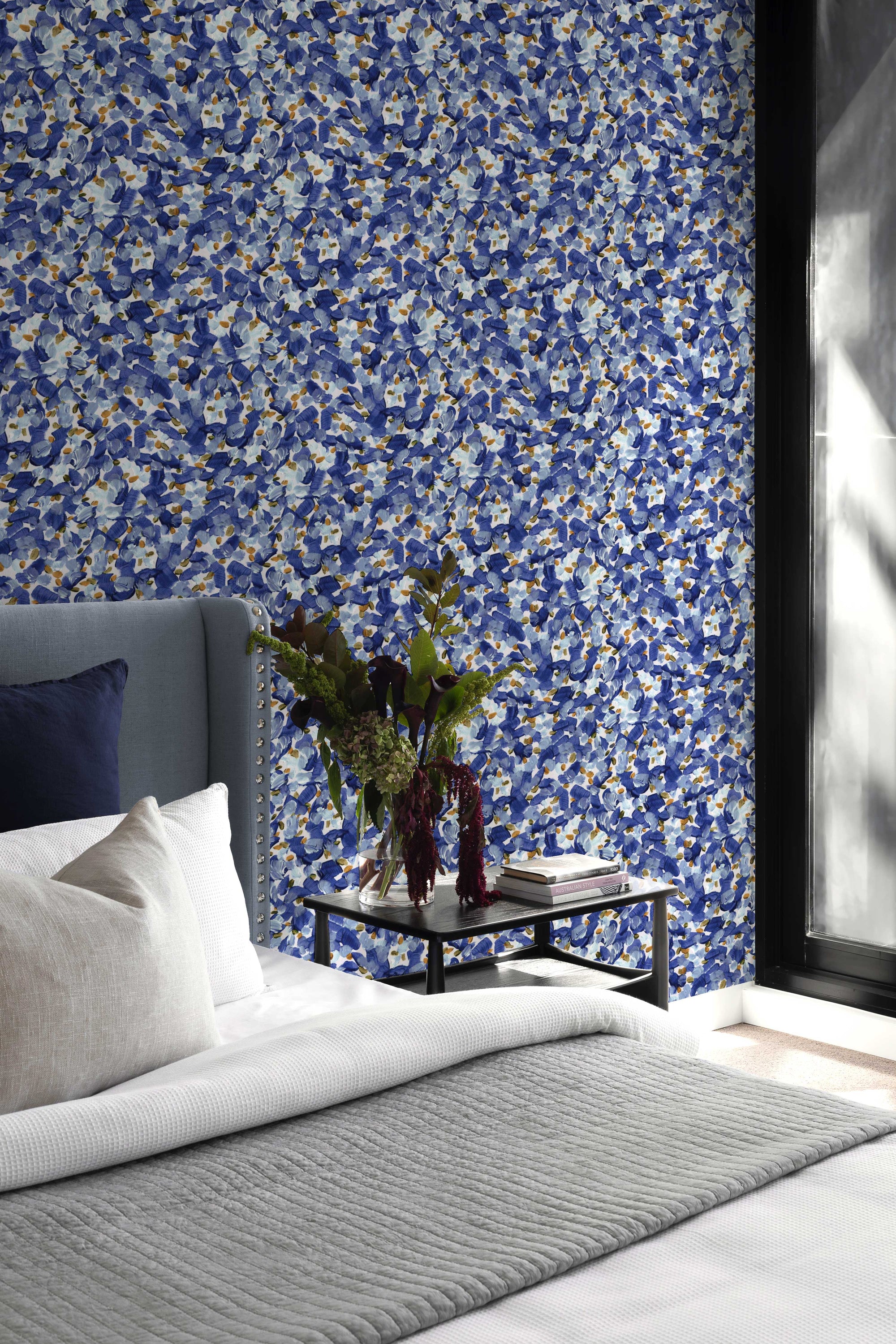 Chintz Moderne abstract floral wallpaper in azure installed in a bedroom with bed and table with flowers