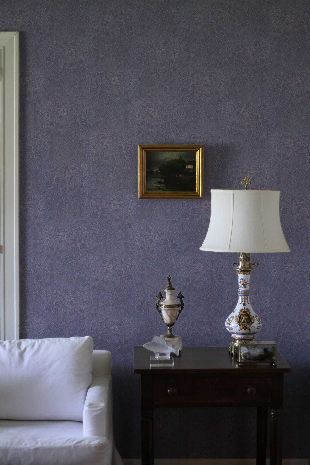 Fiori floral wallpaper in washed denim installed in a living room with picture, lamp, table, and sofa