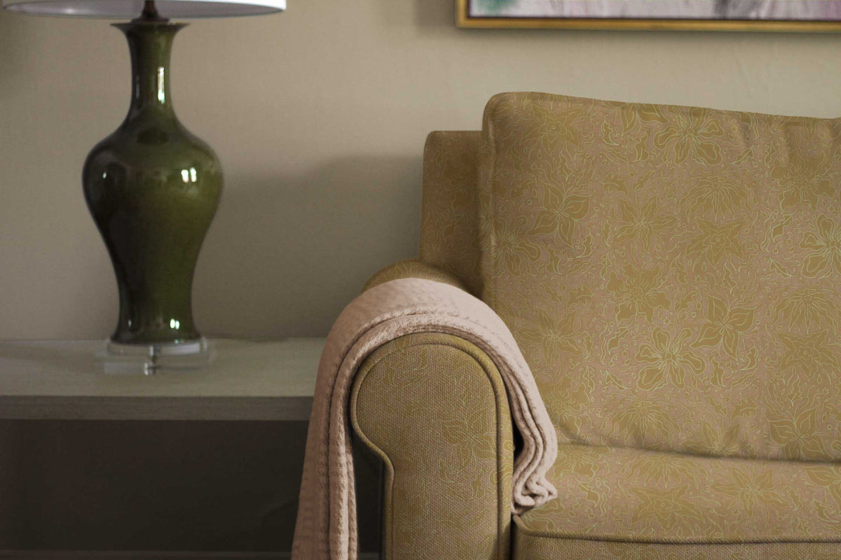 Fiori hand-drawn floral cotton fabric in sulphur yellow upholstered on a sofa and installed in a living room with a lamp and table
