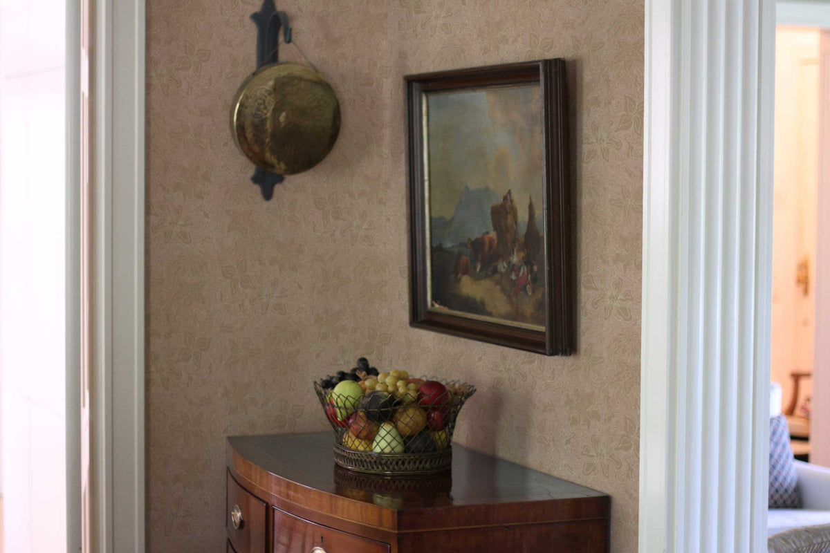 Fiori hand drawn floral wallpaper in neutral nude installed in a living room with framed art, marble fruit basket, and antique dresser