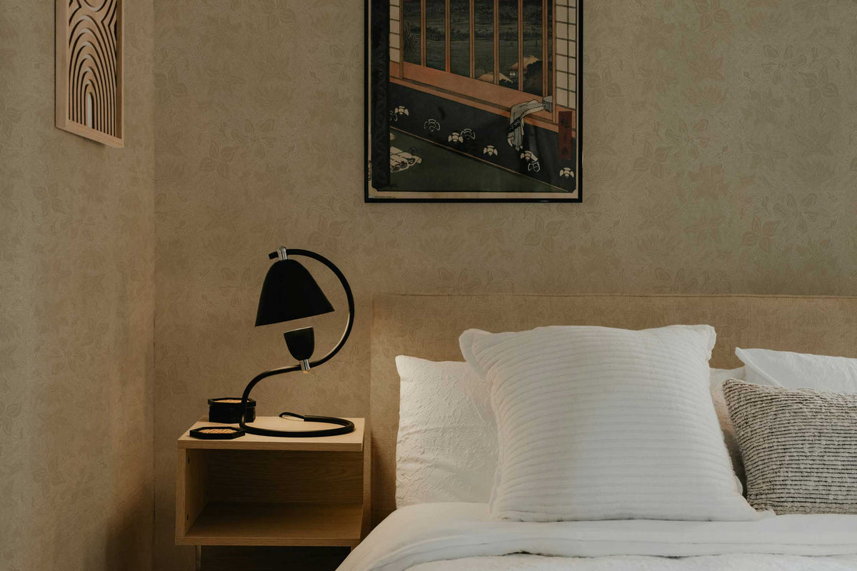Fiori floral wallpaper in taupe installed in a bedroom with bed, bedside table, and art