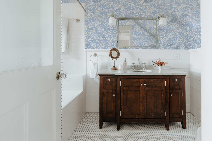 Venable Moore frizzante clay coated wallpaper in pastel ice blue on bathroom walls with wooden vanity and mirror seen through doorway