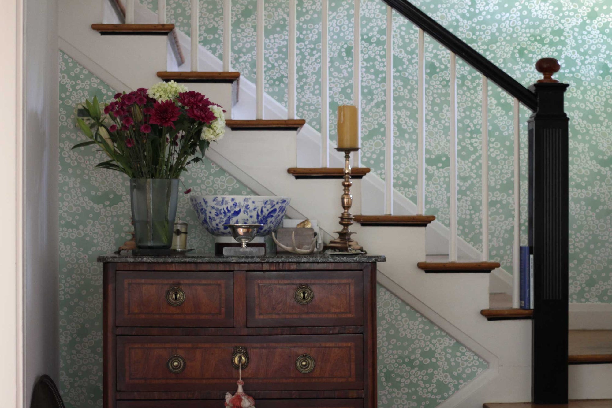 Frizzante dotted wallpaper in verdigris green installed in an entryway with stairs and antique chest with flowers