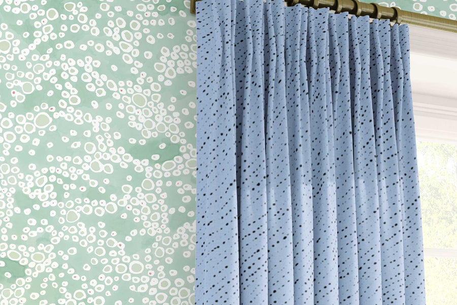 Venable Moore ‘‘Frizzante’ Pastel verdigris green made-to-order, printed in the U.S.A. wallpaper on a wall with 100% European linen “Staccato Nero’ Shibori curtains in sky blue and window 