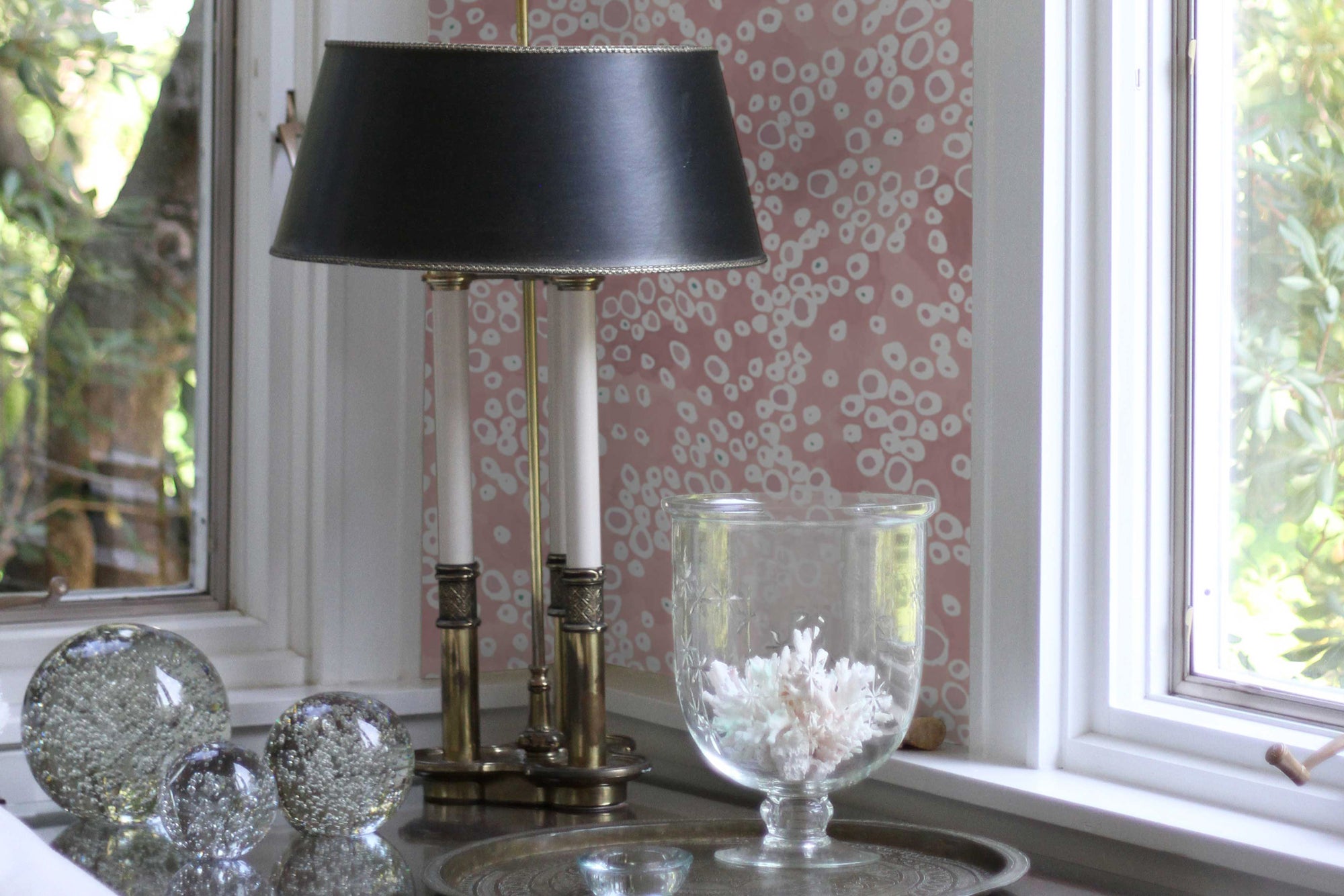 'Frizzante' dotted wallpaper in madder installed in a room with windows, lamp, and glass decorations