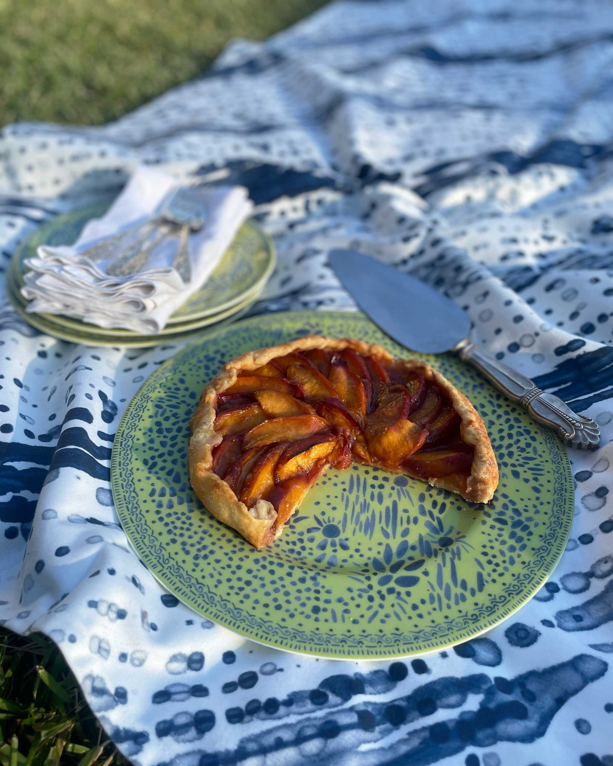 Venable Moore Glissando Shibori cotton marine blue tablecloth on grass with Mosaic Garden apple plate with tart