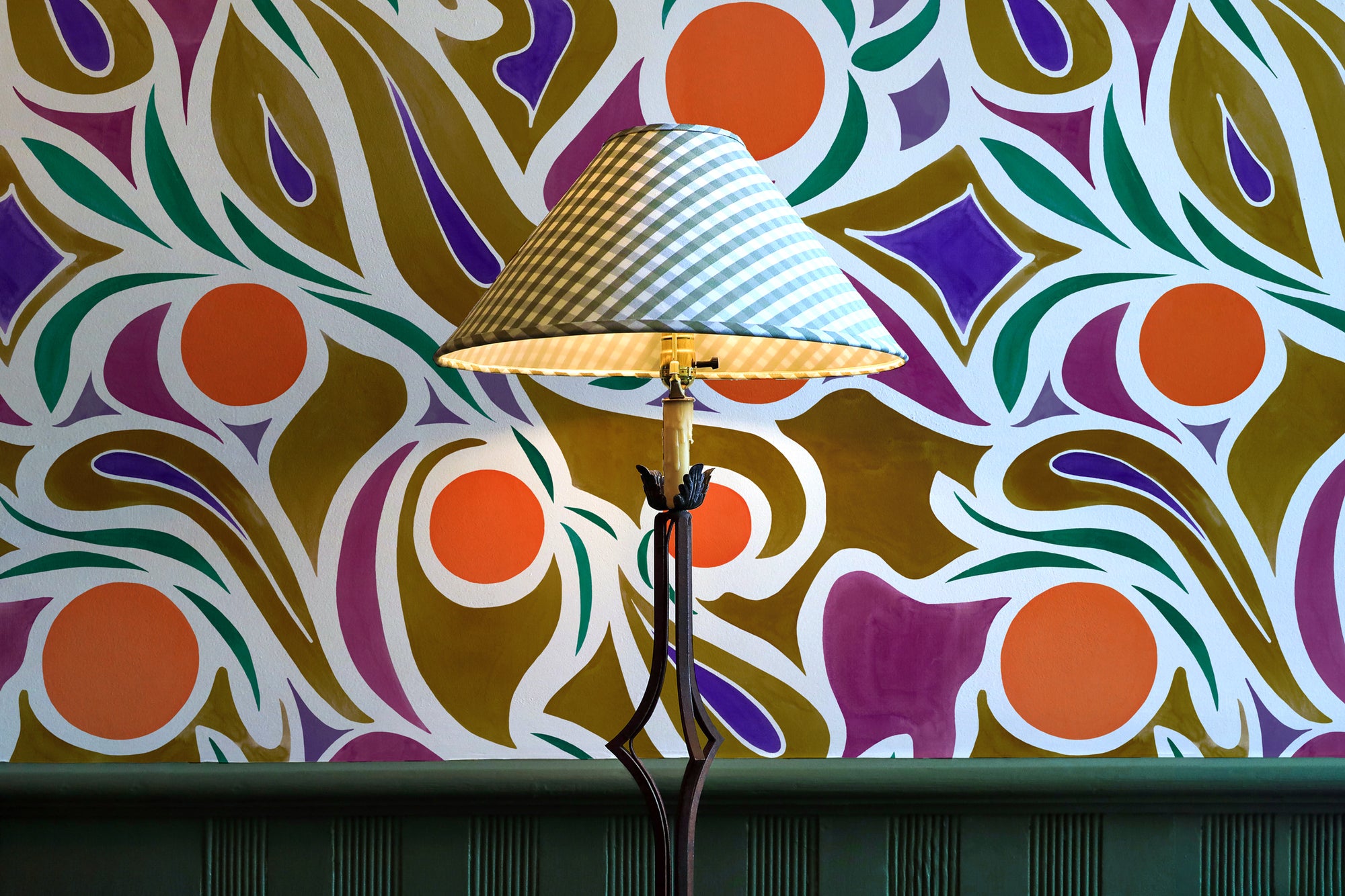 'Capri' abstract floral wallpaper in orange installed in a room with a lamp and wainscotting