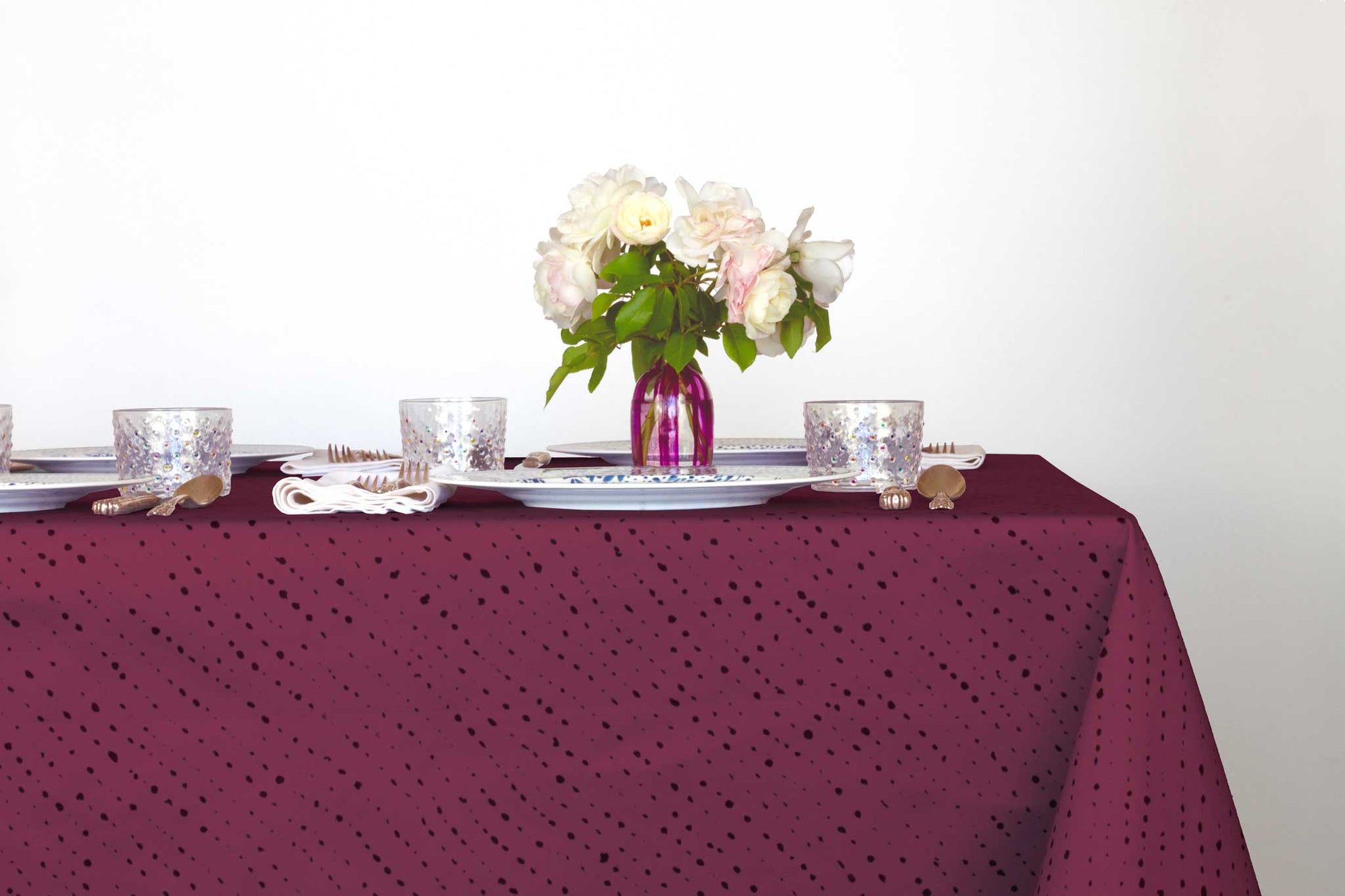 Venable Moore Staccato Nero shibori 100% cotton tablecloth in cerise on table with mosaic garden dinner plates, hand-painted confetti glasses and vase with roses 