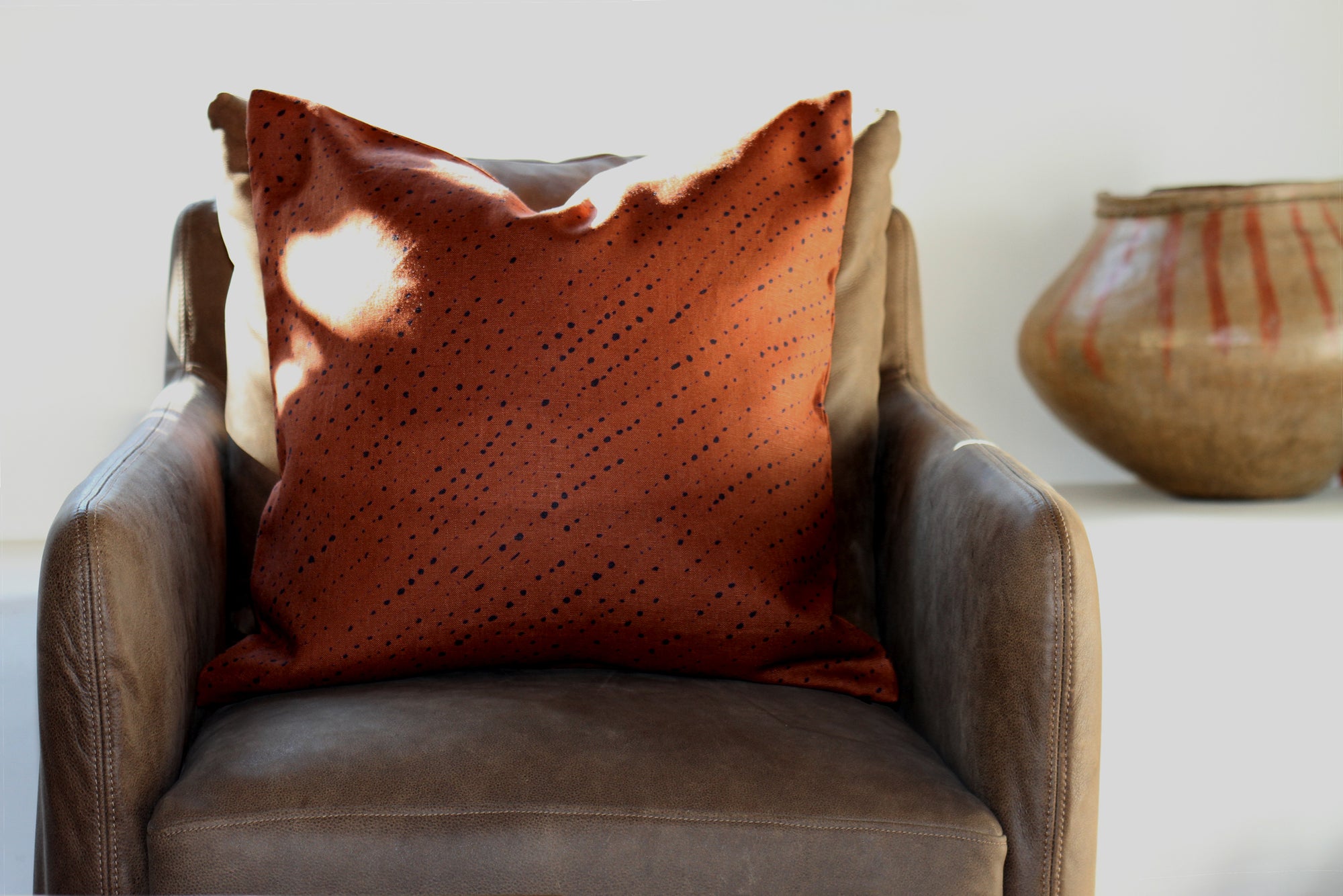 'Staccato Nero' Shibori linen pillow in russet on chair with pot in background