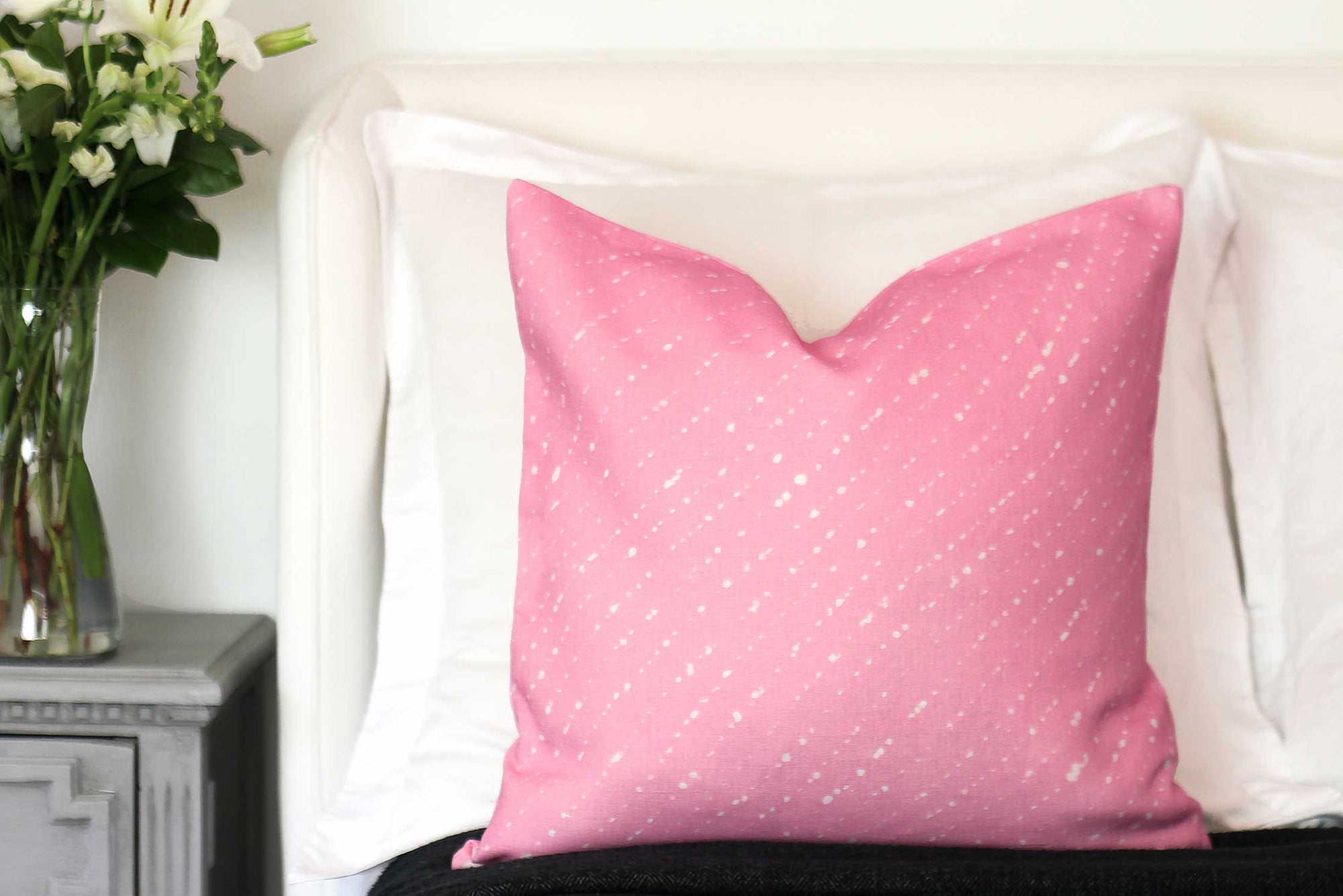 Venable moore staccato sbiancato shibori linen pillow in carnation pink on a bed with white shams and flowers on bedside table