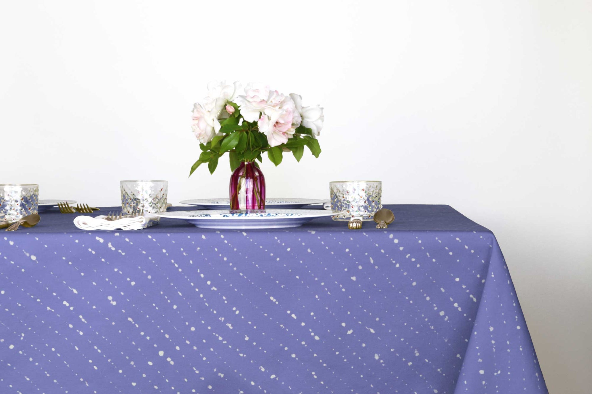 Staccato sbiancato shibori cotton tablecloth in cornflower on table with mosaic garden dinner plates and hand-painted confetti glasses and vase with roses