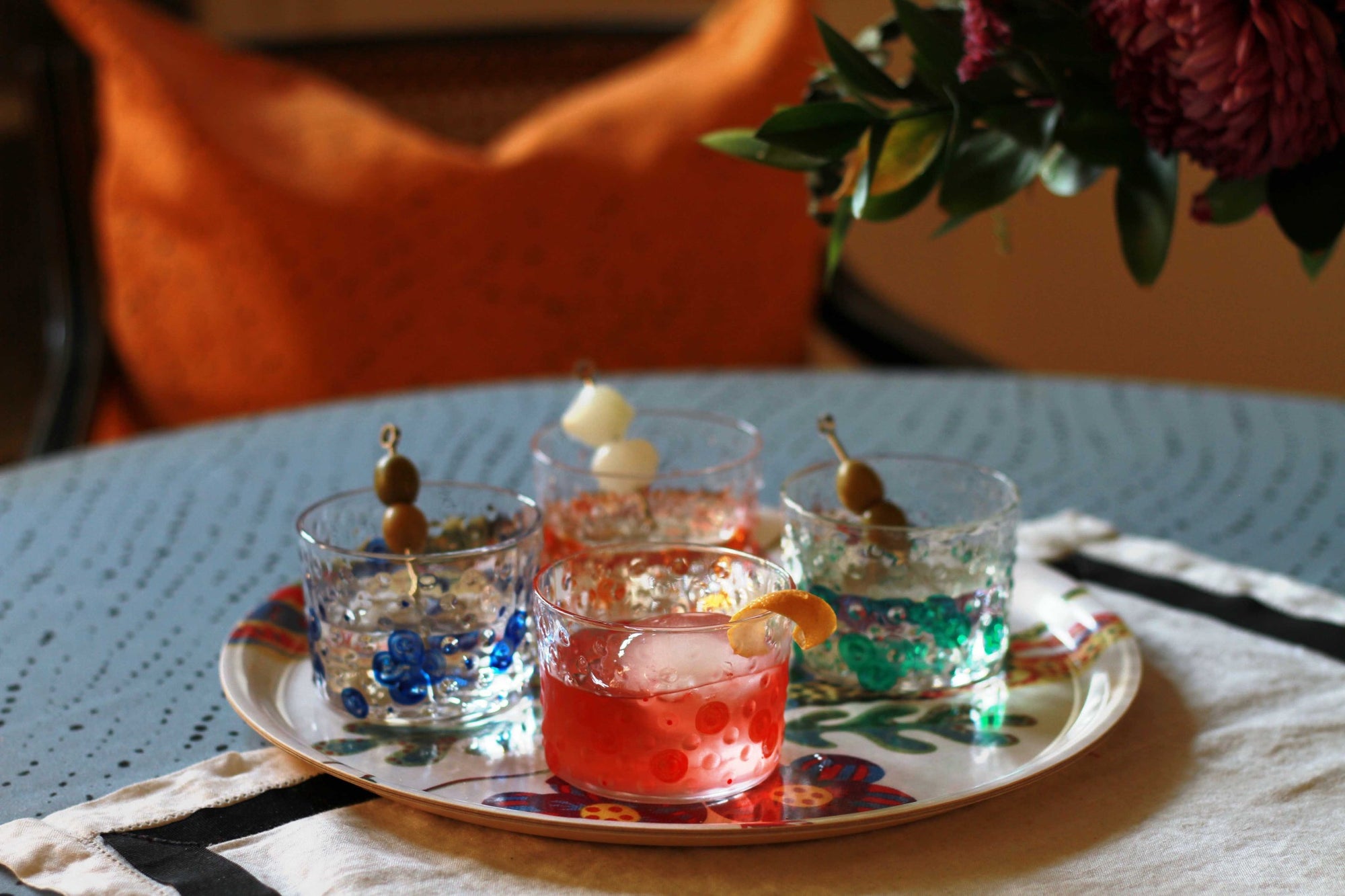 Venable Moore Shamrock green, Tangerine orange, Tomato red, lapis blue hand-painted Bubble glasses on a tray on a table with flowers