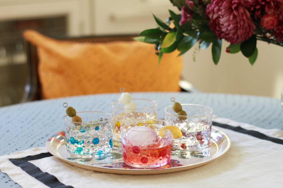Venable Moore Sun yellow, Turquoise blue, Magenta pink, and Coffee brown hand-painted Bubble glasses on a tray on a table with flowers