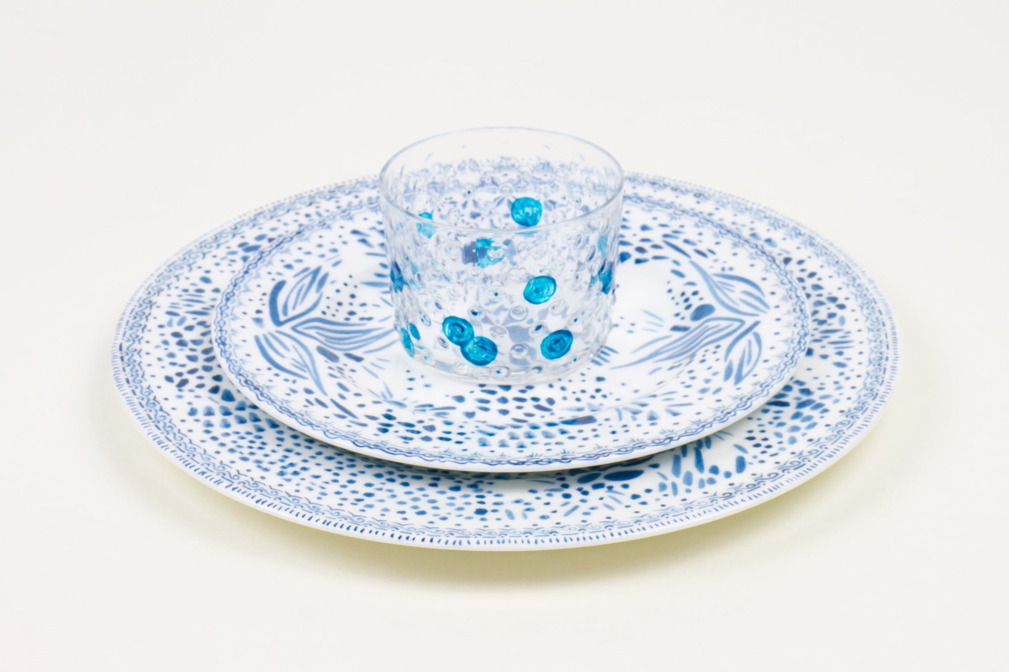 Place setting of hand-painted turquoise glass stacked on blueberry mosaic garden salad and dinner porcelain plates