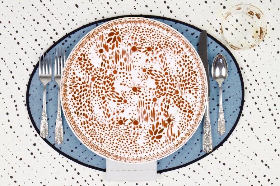 Venable Moore Mosaic Garden dinner plate in chestnut brown with hand-painted Bubble glass on sky blue 'Staccato Neroo' Shibori linen placemat and alabaster white tablecloth with silverware and white linen napkin