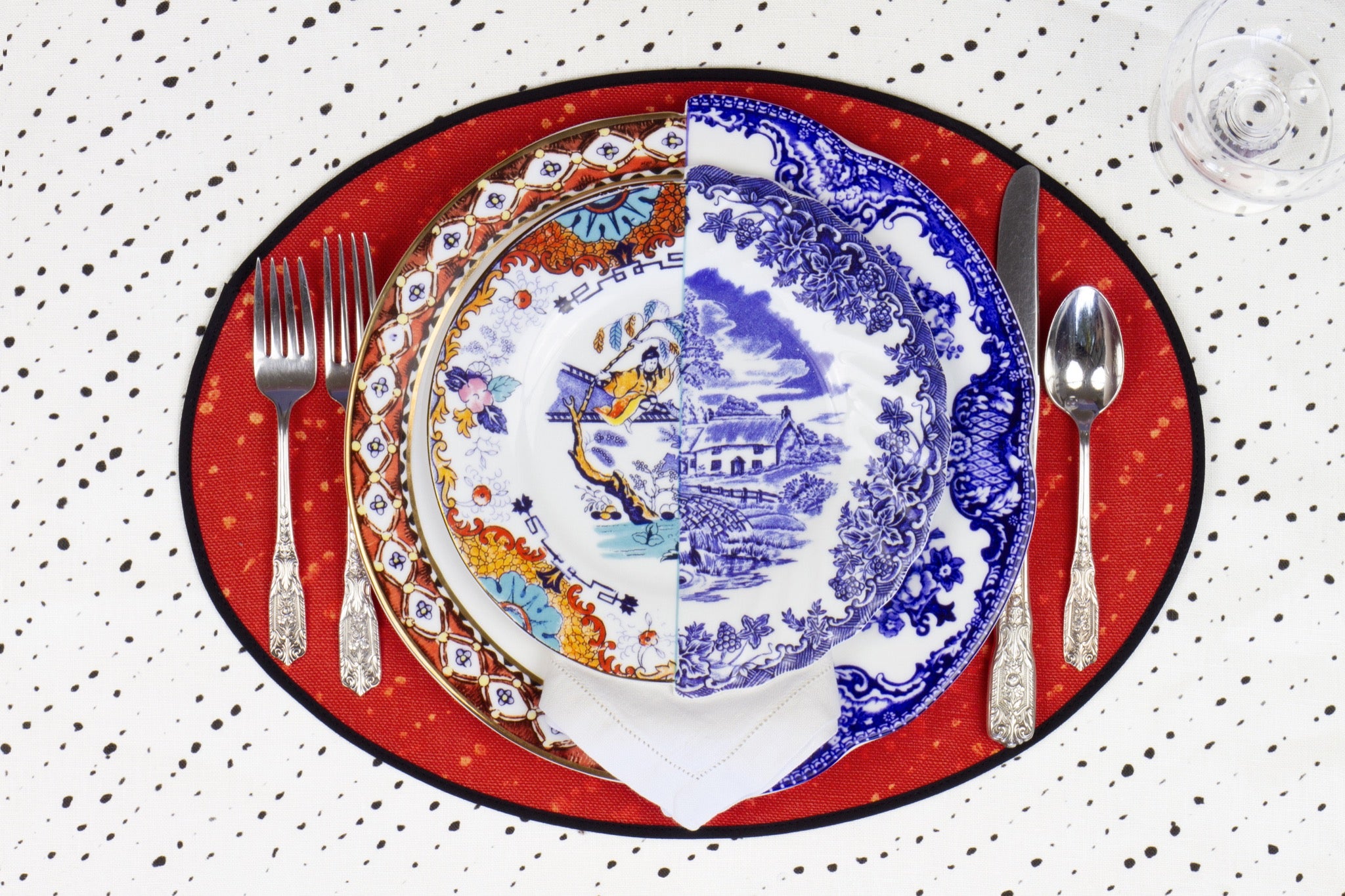 Place setting with 100% linen staccato decolorato shibori paprika red placemat on alabaster shibori with colored plates